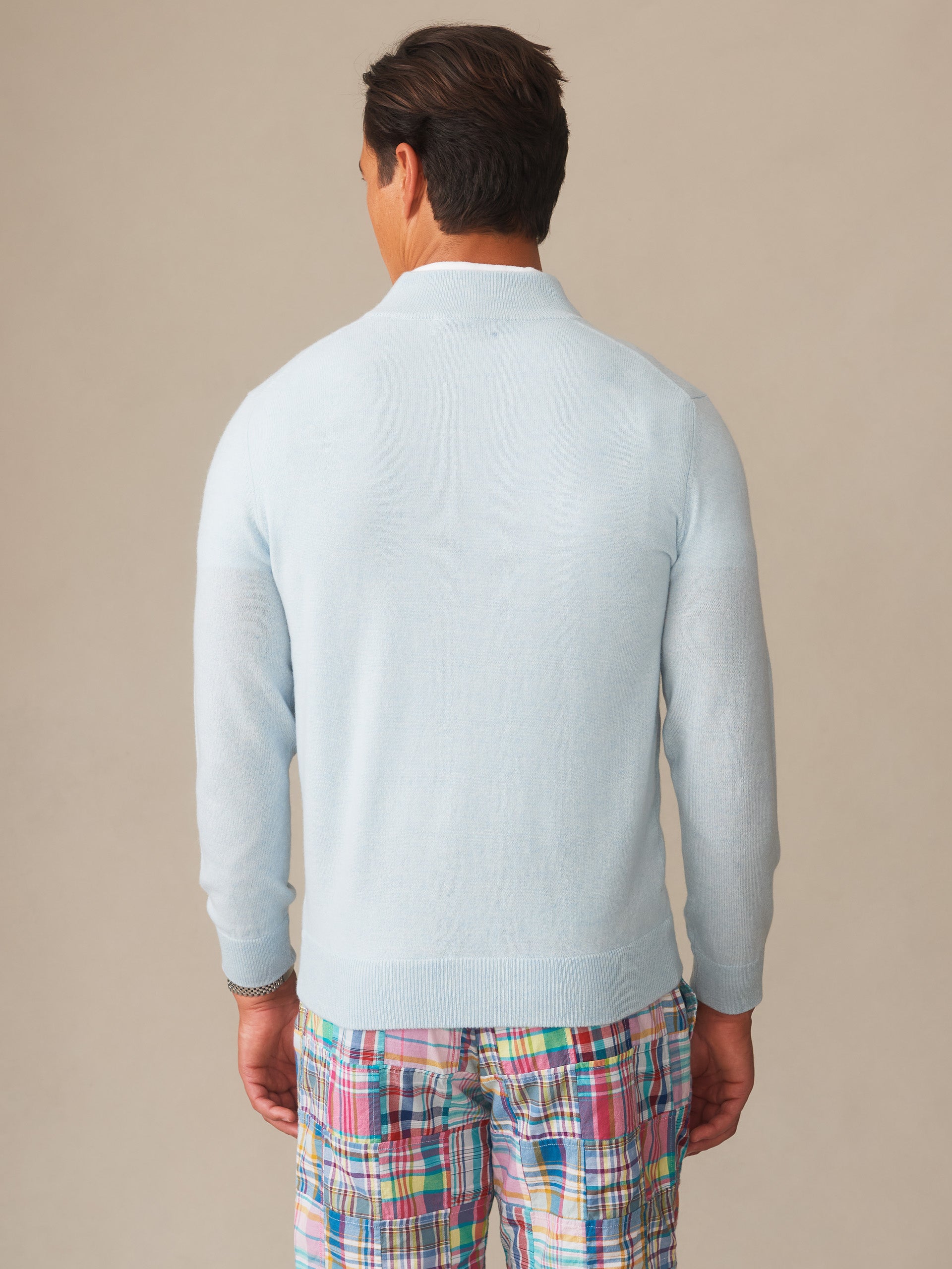 Man wearing a light blue Twain Cashmere 1/4 Zip sweater by J.McLaughlin paired with colorful plaid shorts, showcasing effortlessly stylish, enduring designs and an innovative fabric blend.