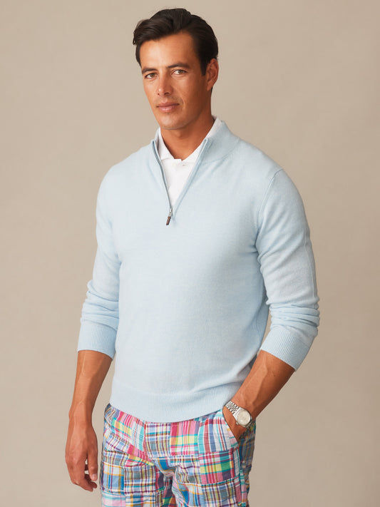 Man wearing a light blue Twain Cashmere 1/4 Zip sweater by J.McLaughlin over a white shirt paired with colorful plaid pants, showcasing effortlessly stylish and enduring designs.