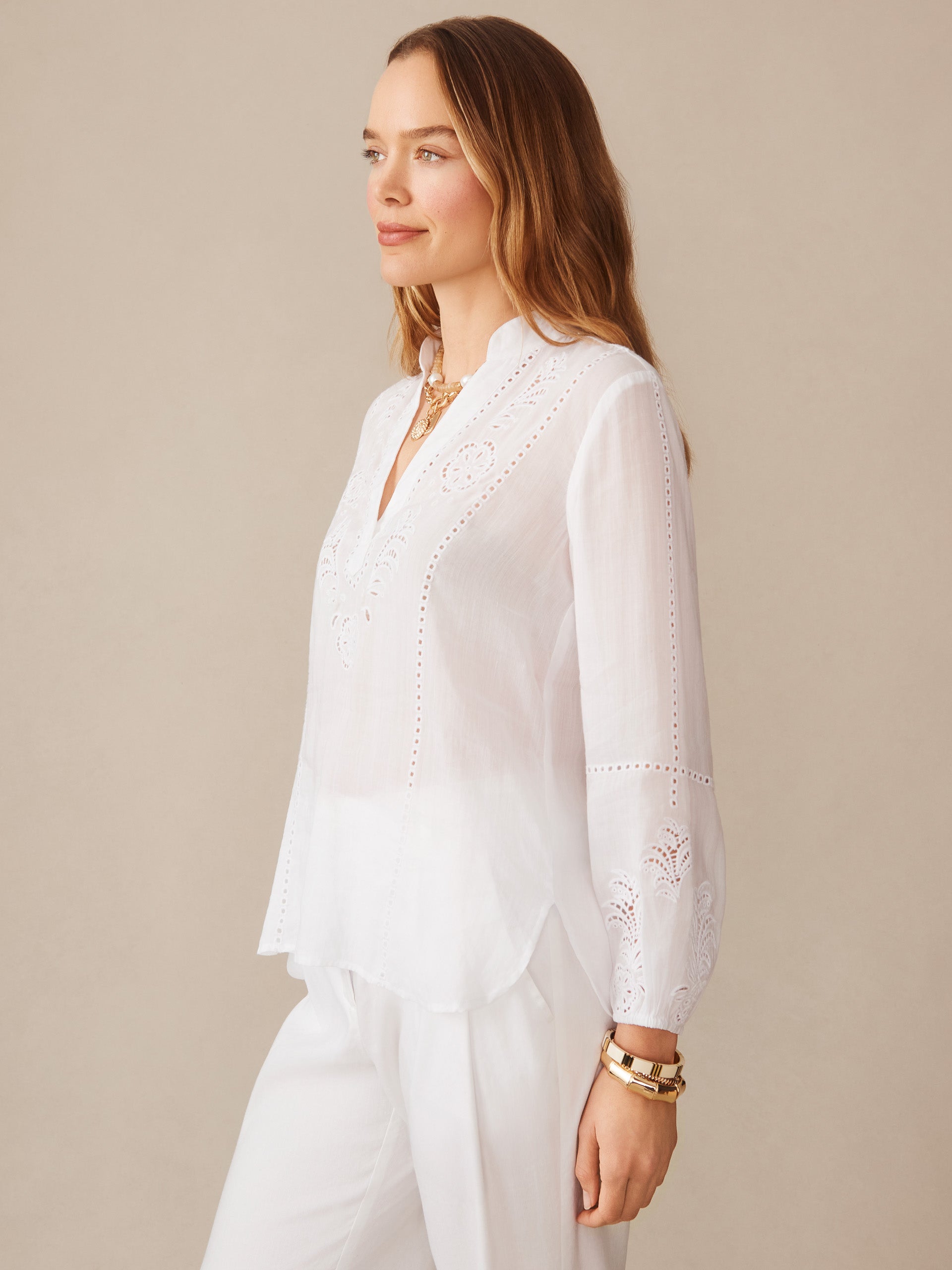 Woman wearing a white Varsha Blouse by J.McLaughlin featuring delicate embroidery and eyelet details, styled with white pants and gold bracelets for a timeless, elegant look.