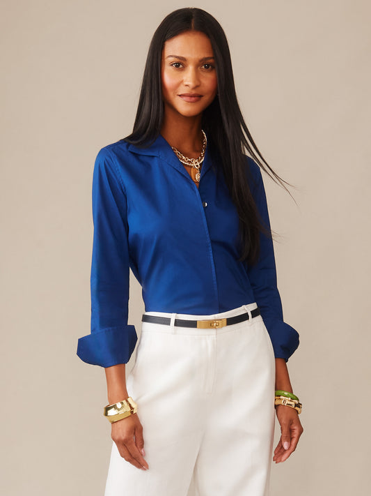 Woman wearing a navy Victoria Shirt by J.McLaughlin paired with white pants and gold accessories, showcasing effortlessly stylish, enduring designs in a legacy of timeless fashion.