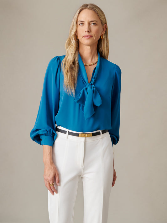 J.McLaughlin Vienna Blouse in blue with a scarf tie neckline and voluminous sleeves styled with white pants