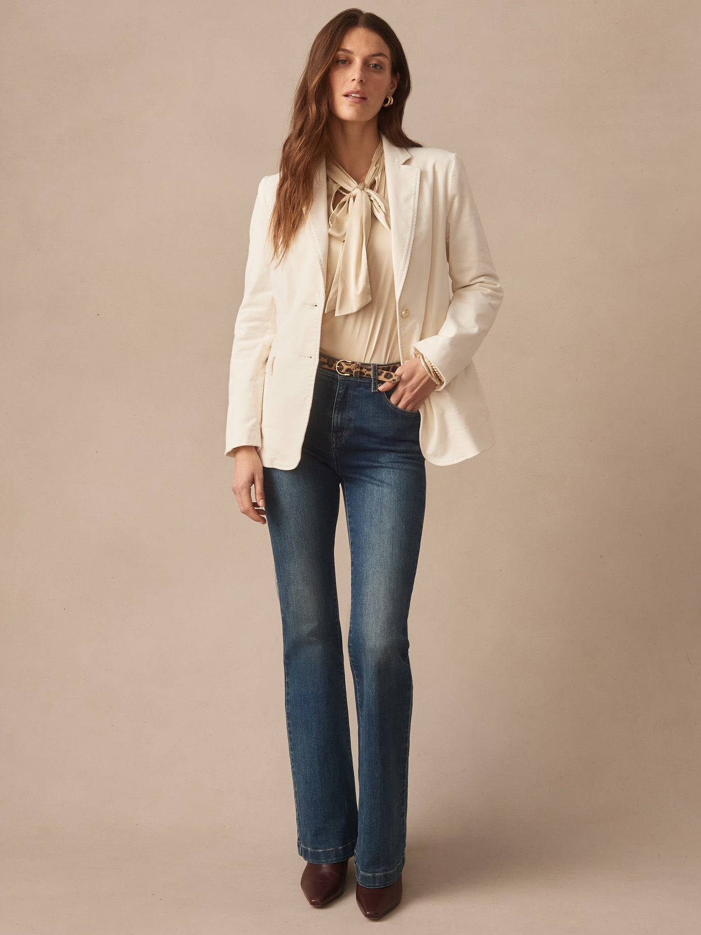 Woman wearing an effortlessly stylish Ivette Velvet Blazer by J.McLaughlin in a neutral shade paired with a blouse and jeans, showcasing enduring designs and innovative fabrics.