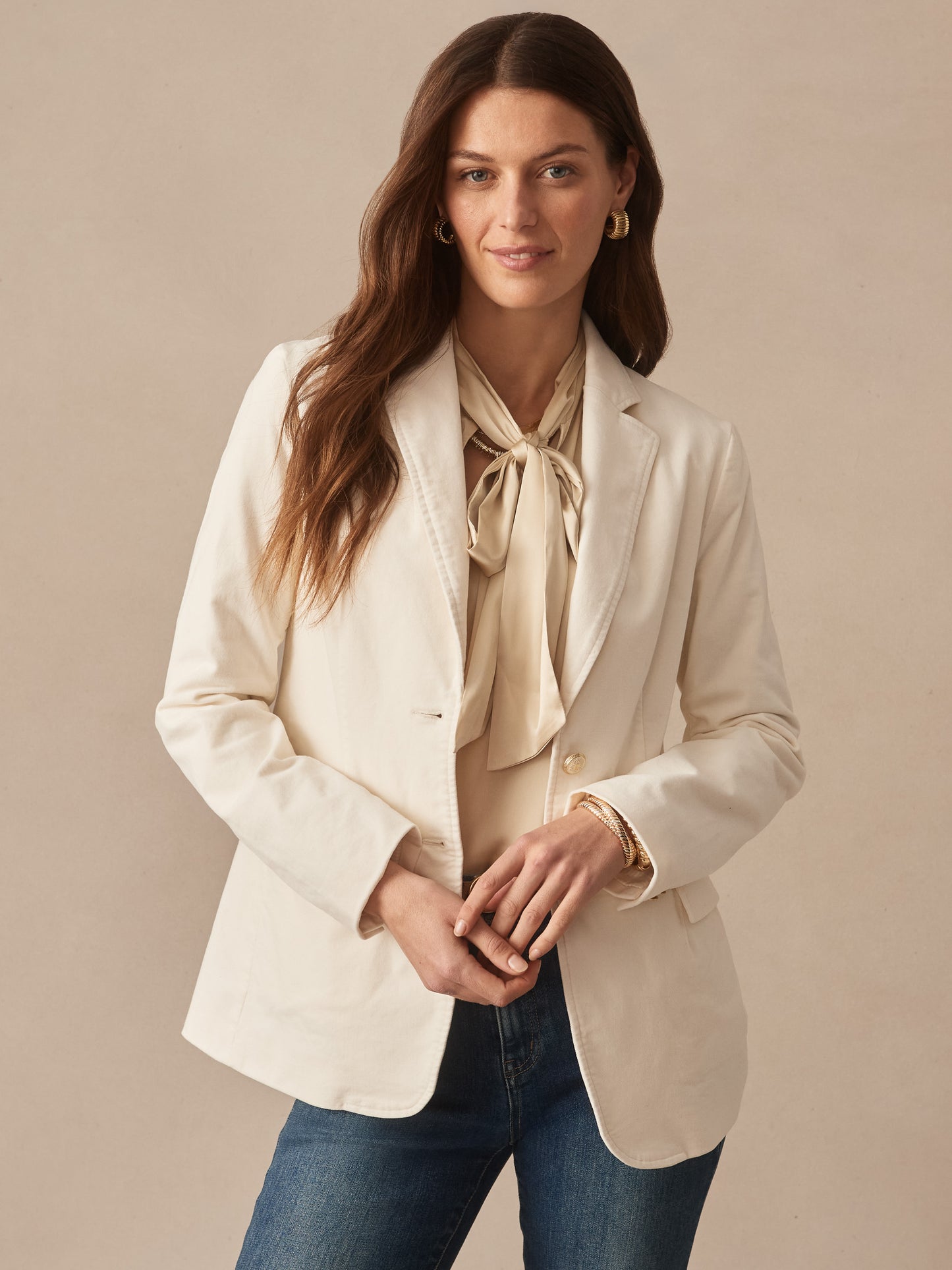 Woman wearing the Ivette Velvet Blazer by J.McLaughlin in a soft champagne tone paired with a silky blouse and jeans, showcasing effortlessly stylish, enduring designs and innovative fabrics.