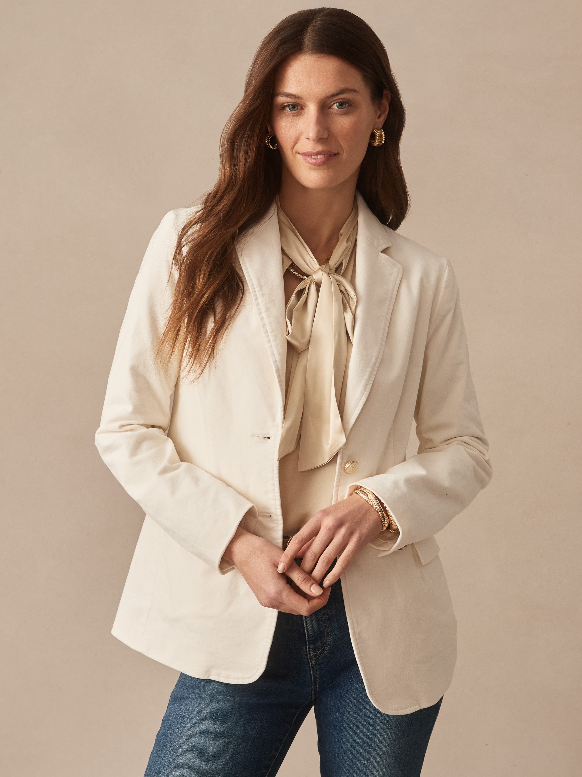 Woman wearing the Ivette Velvet Blazer by J.McLaughlin in a soft champagne tone paired with a silky blouse and jeans, showcasing effortlessly stylish, enduring designs and innovative fabrics.