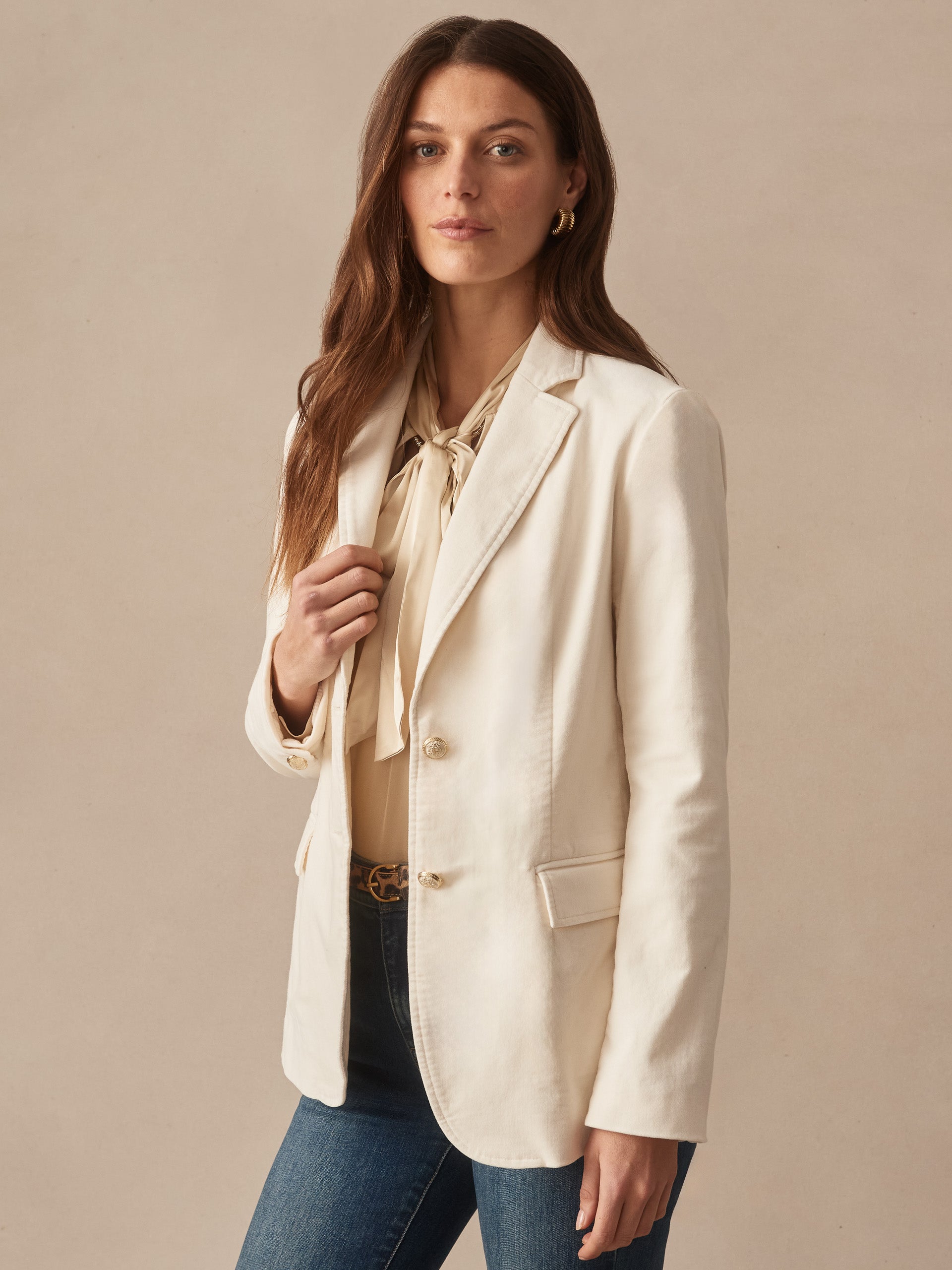 Woman wearing an effortlessly stylish Ivette Velvet Blazer by J.McLaughlin in a soft champagne hue, paired with a blouse and jeans, showcasing enduring designs and timeless fashion.