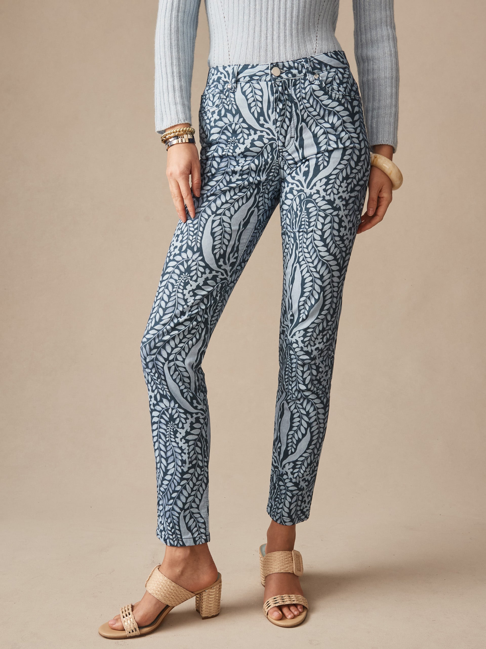 Woman wearing patterned blue pants and beige heeled sandals paired with a ribbed grey sweater and bracelets, showcasing J.McLaughlin's Watson Cotton Cashmere Pants in Coral Current, epitomizing effortlessly stylish, enduring designs with a legacy of timeless fashion. A destination for defining style. Life, Well-Lived.