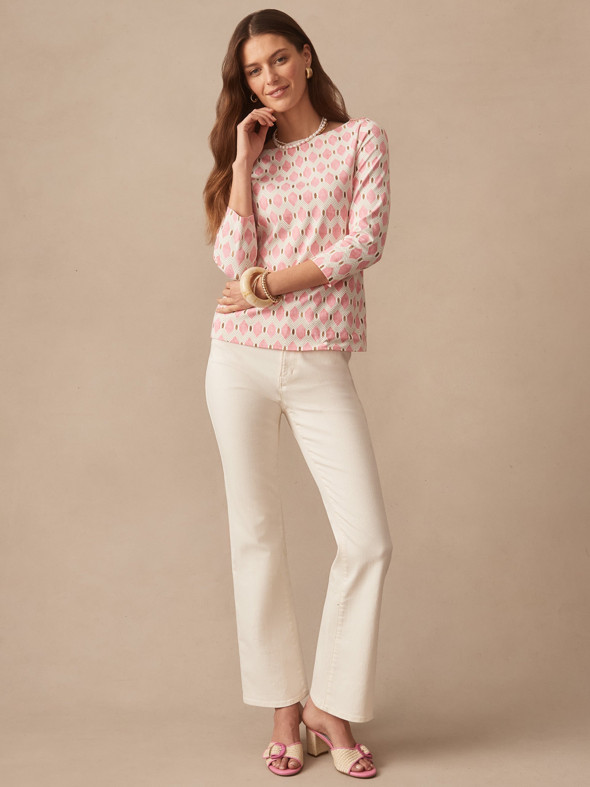 Woman wearing the Wavesong Tee in Mini Beekeeper by J.McLaughlin, featuring a pink and tan patterned top paired with white pants and stylish sandals, showcasing effortlessly stylish, enduring designs with innovative fabrics. A destination for defining style. Life, Well-Lived.
