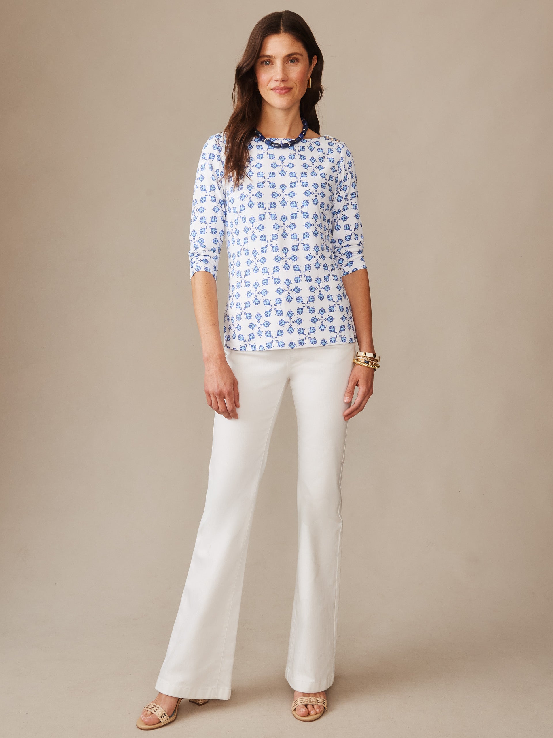 Woman wearing a Wavesong Tee in Mythic Tile by J.McLaughlin, featuring a blue floral pattern on a white fabric, paired with white pants and gold accessories, embodying effortlessly stylish and enduring designs.