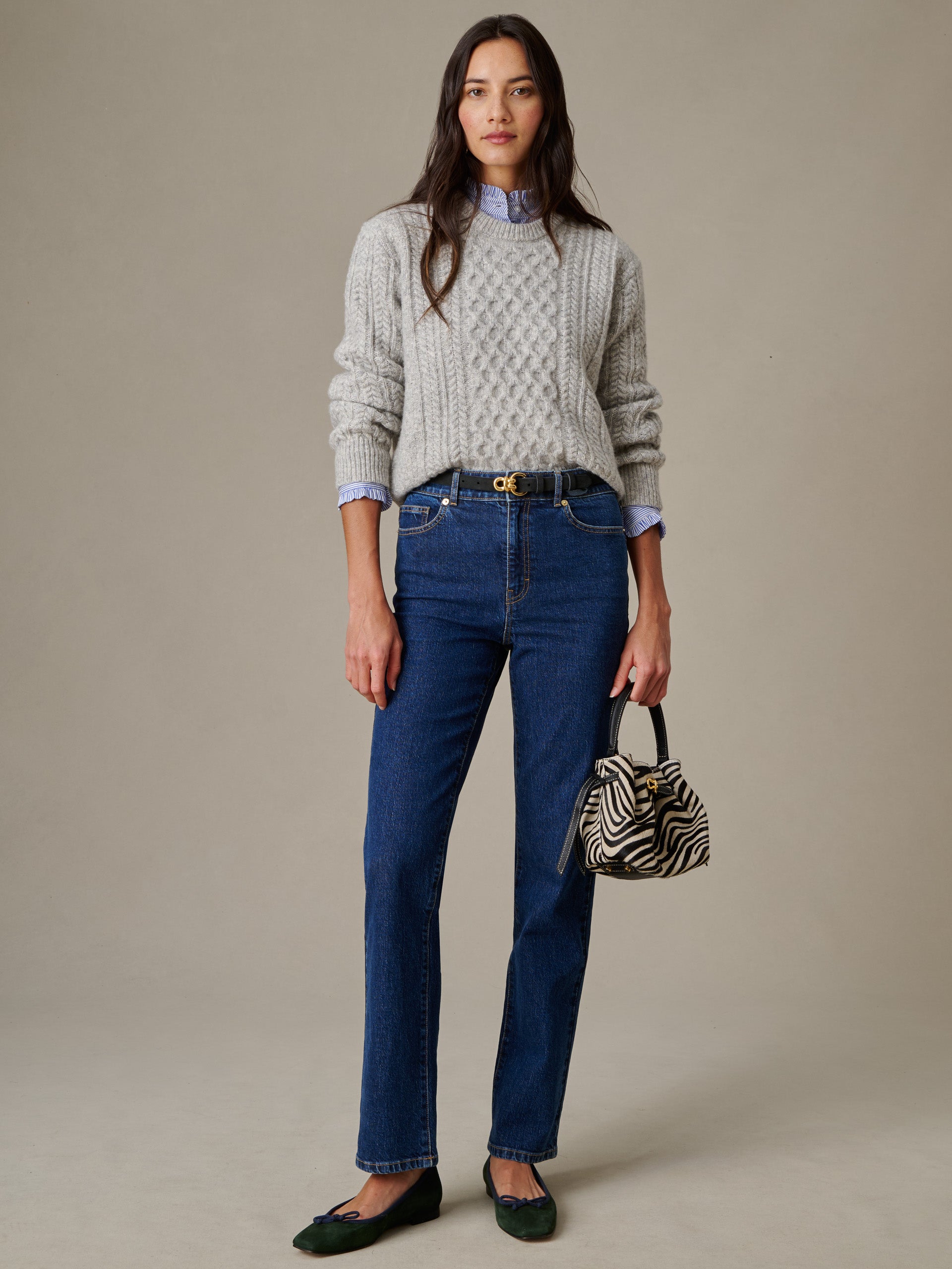 Woman wearing Willow Jeans by J.McLaughlin paired with a grey cable-knit sweater, holding a zebra-print handbag, showcasing timeless, effortlessly stylish, enduring denim.