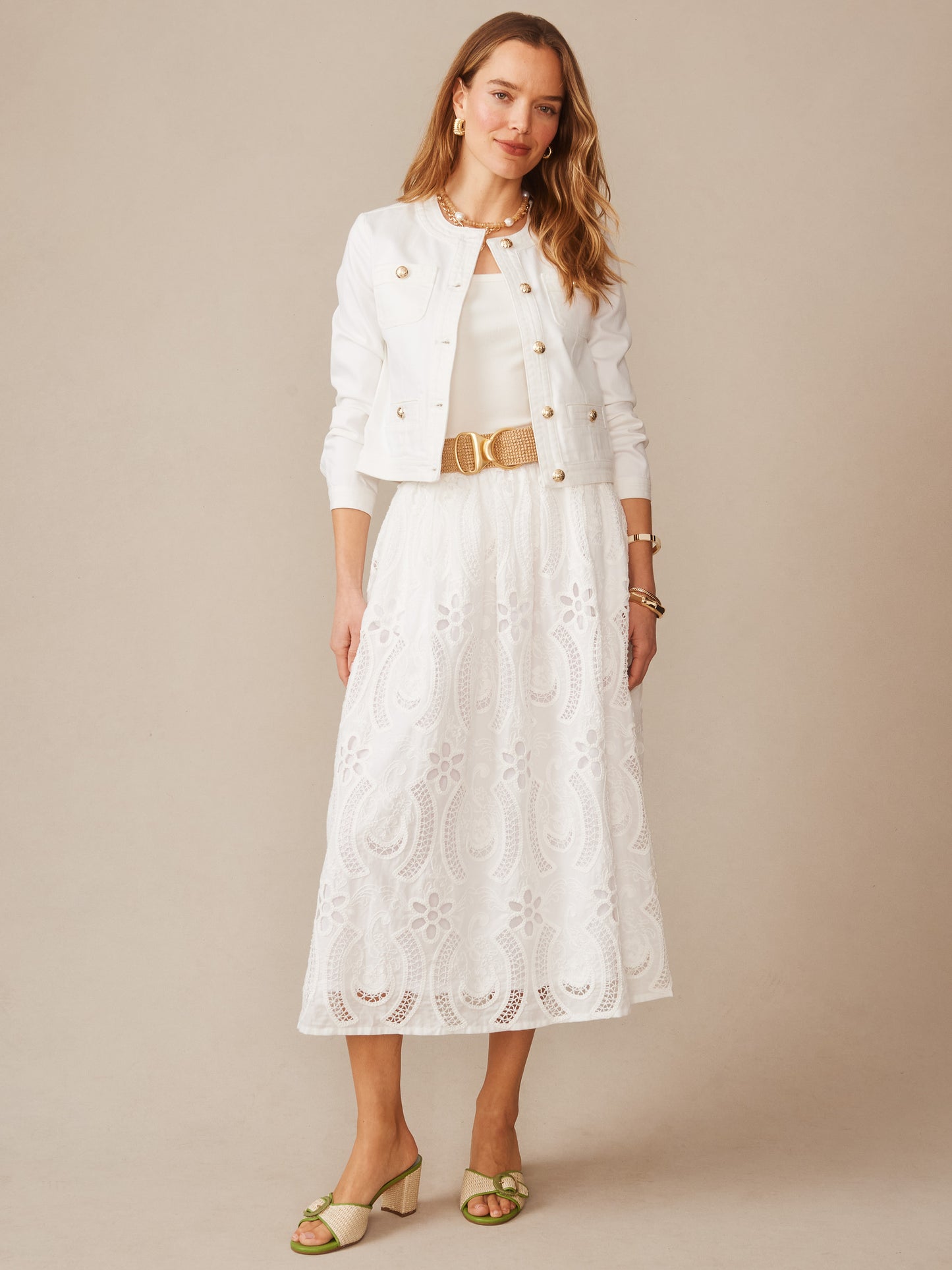 Woman wearing a white Winnie Skirt in Eyelet with intricate lace detailing paired with a white jacket and beige belt, showcasing J.McLaughlin’s effortlessly stylish, enduring designs.