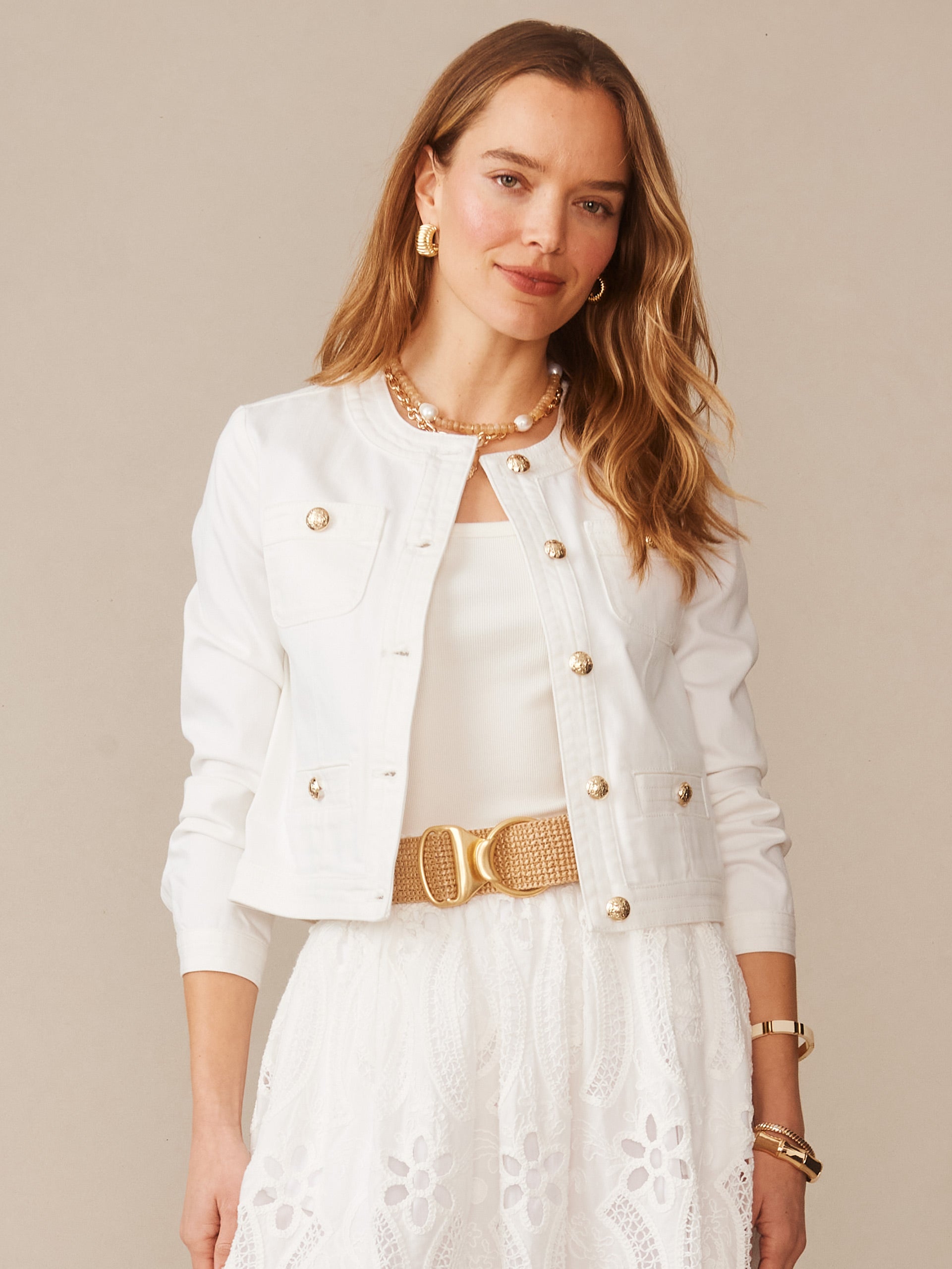 Woman wearing a white Jackie Denim Jacket by J.McLaughlin paired with a white top and eyelet skirt, showcasing effortlessly stylish, enduring designs and a legacy of timeless fashion.