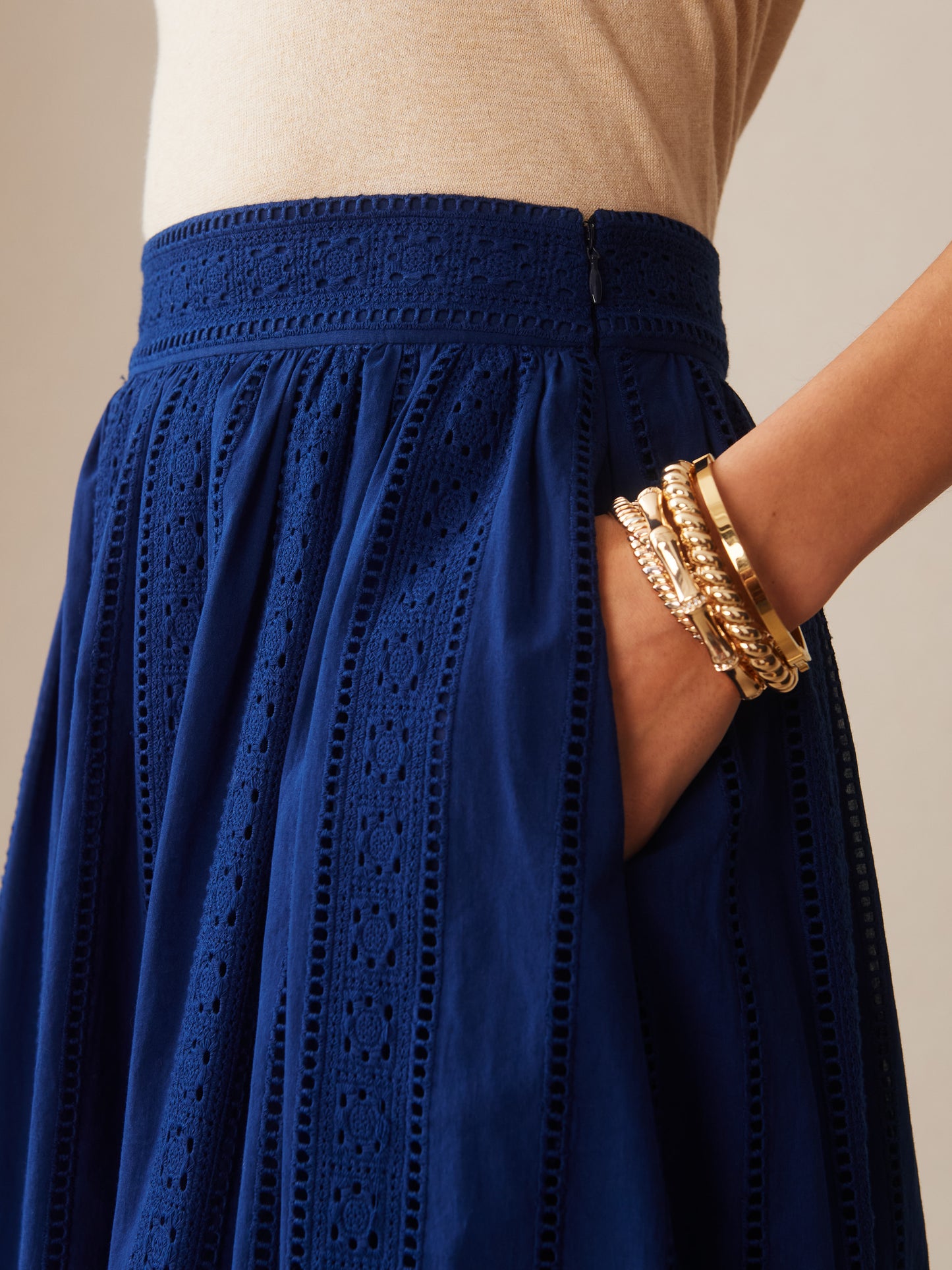Close-up of a woman wearing the Winnie Skirt in Eyelet by J.McLaughlin in navy blue, featuring detailed eyelet fabric and accessorized with gold bracelets, showcasing effortlessly stylish, enduring designs.
