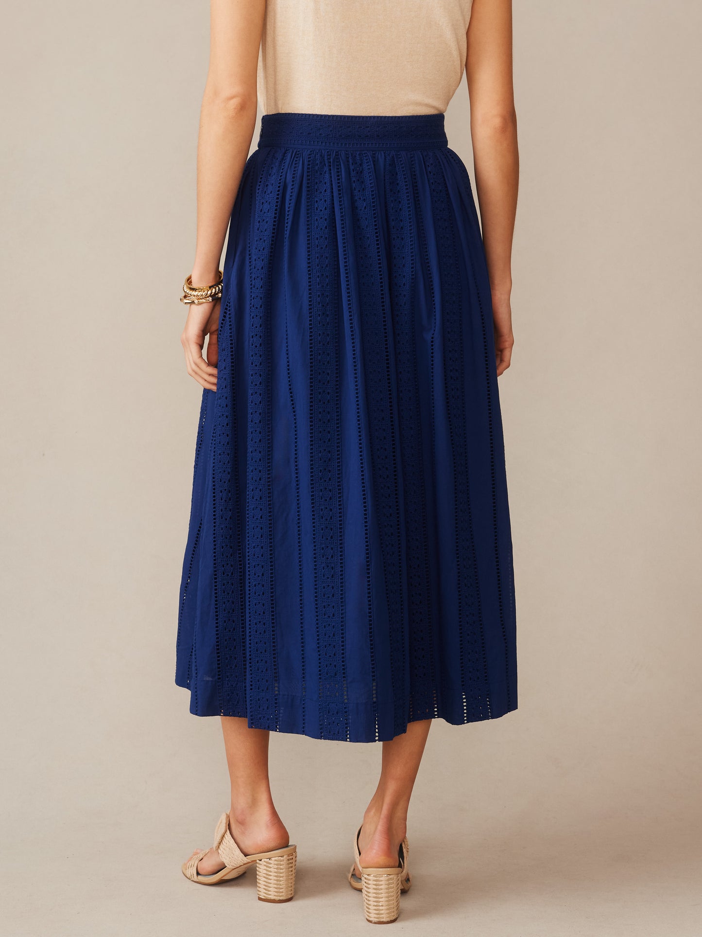 A back view of a woman wearing the Winnie Skirt in Eyelet by J.McLaughlin, featuring a navy blue eyelet fabric and a comfortable waistband, embodying effortlessly stylish, enduring designs with innovative fabrics. A destination for defining style. Life, Well-Lived.