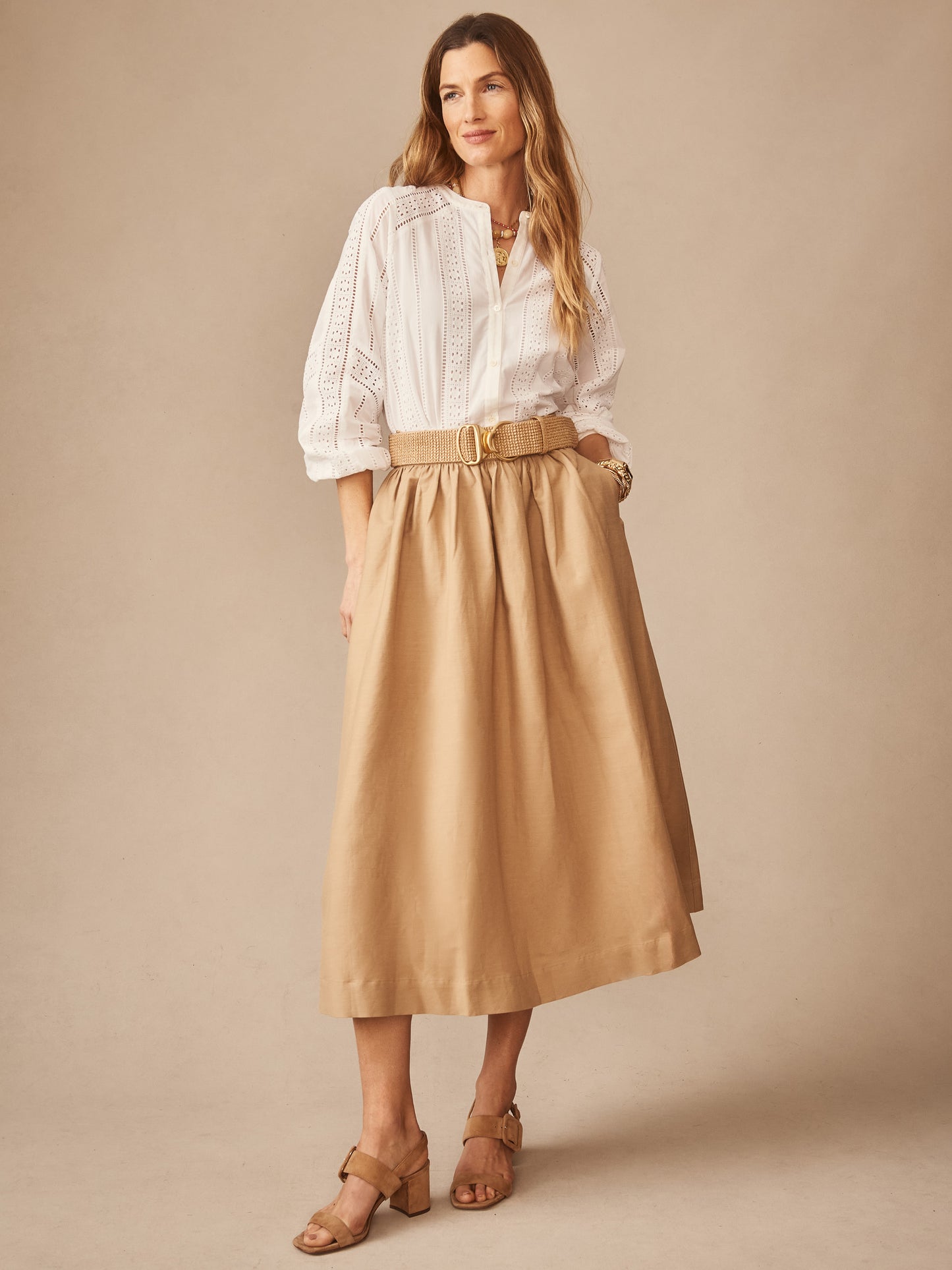 Woman wearing a Winnie Linen Blend Skirt by J.McLaughlin in a neutral tone paired with a white eyelet blouse and tan heeled sandals, embodying effortlessly stylish, enduring designs.