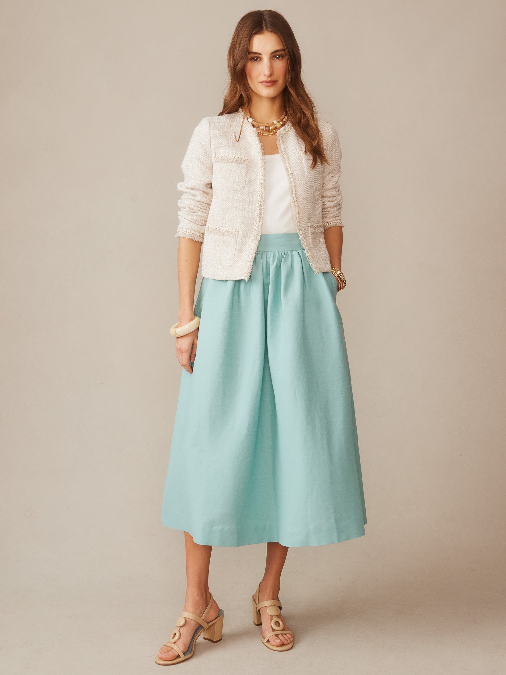 Woman wearing a seafoam green Winnie Linen Blend Skirt from J.McLaughlin paired with a white top, cream textured jacket, and beige sandals, showcasing effortlessly stylish, enduring designs.