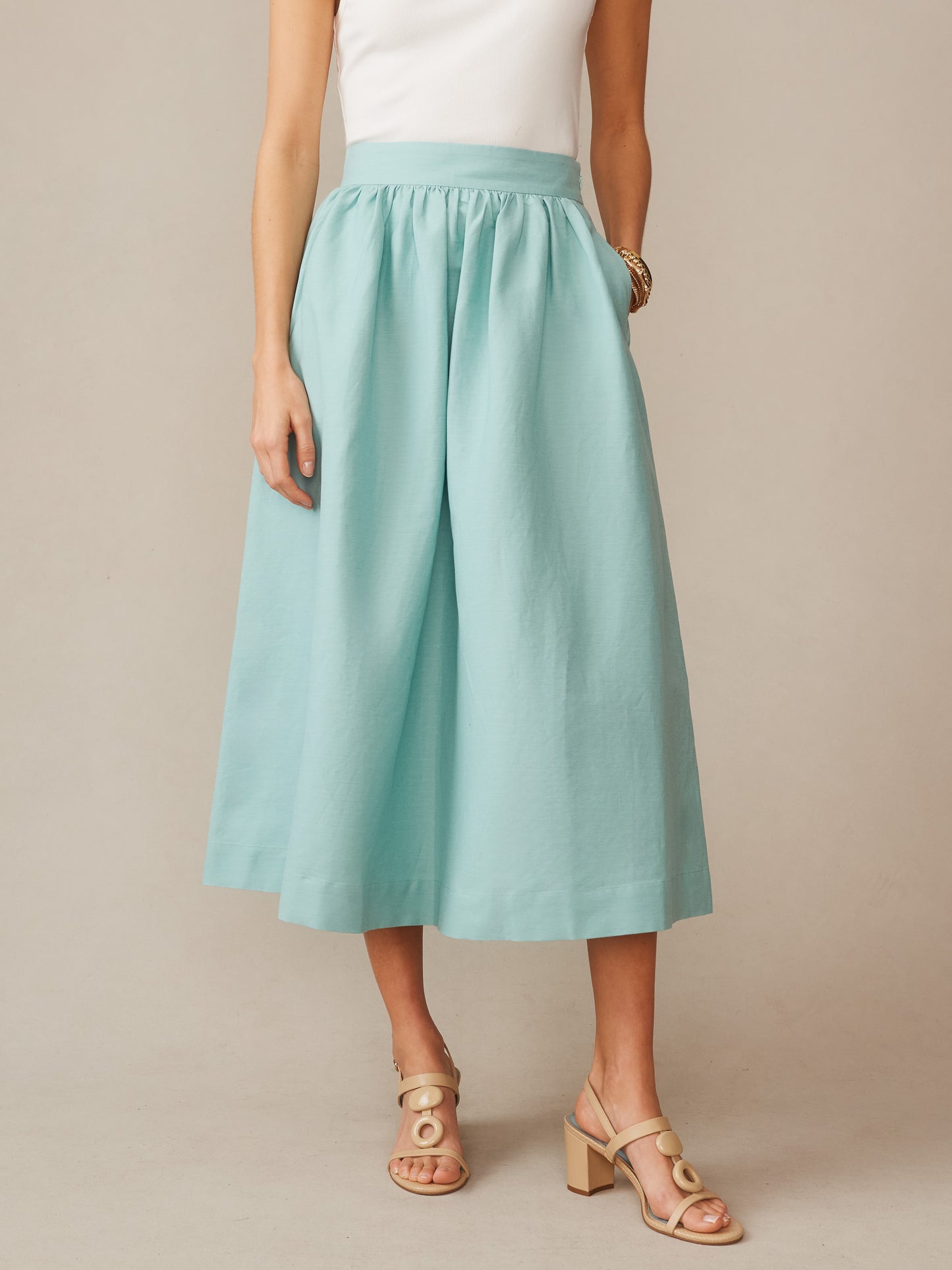 Woman wearing seafoam green Winnie Linen Blend Skirt by J.McLaughlin paired with a white sleeveless top and beige heeled sandals, showcasing effortlessly stylish, enduring designs in linen fabric.