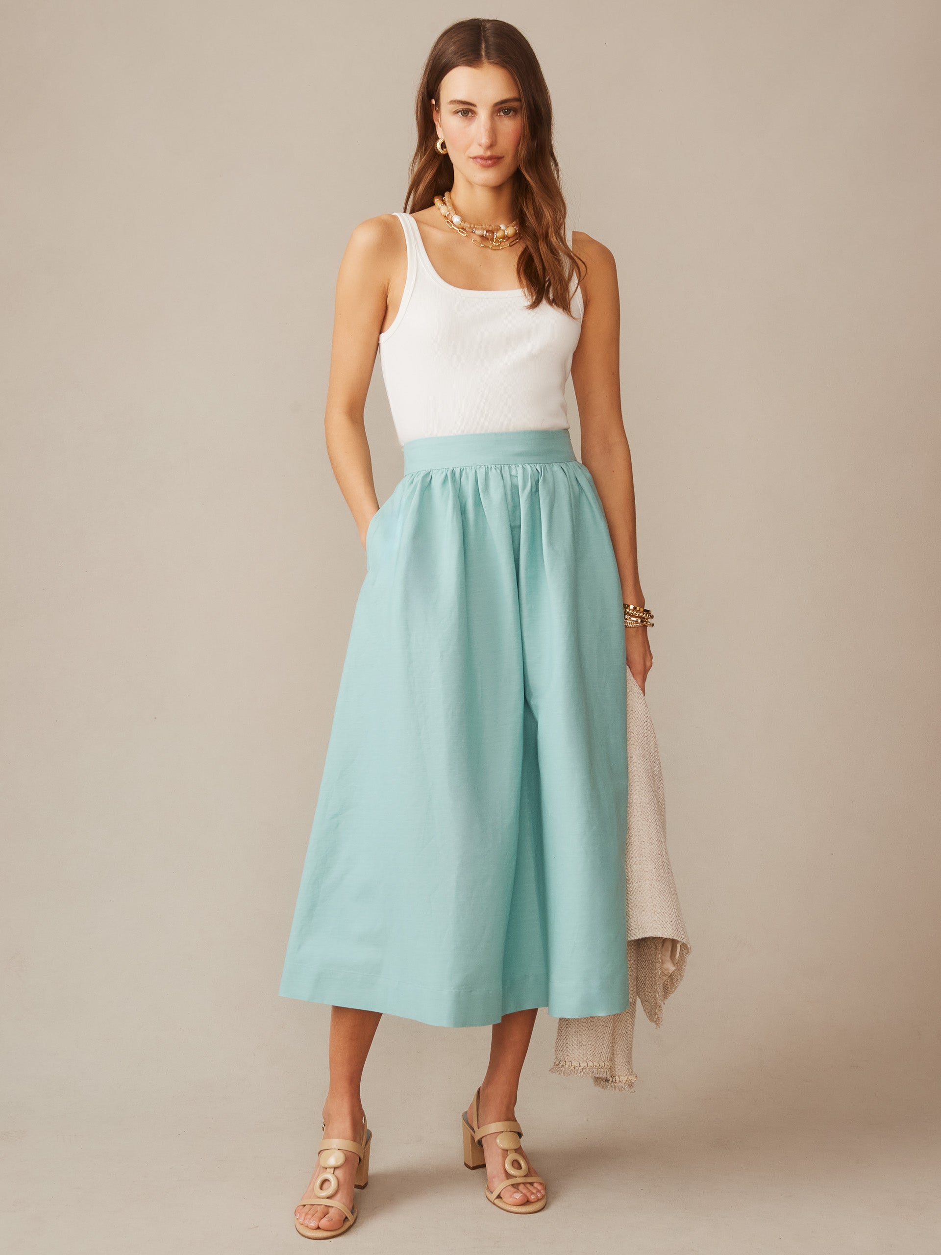 Woman wearing a seafoam Winnie Linen Blend Skirt by J.McLaughlin paired with a white tank top and beige sandals, showcasing effortlessly stylish, enduring designs in timeless fashion.