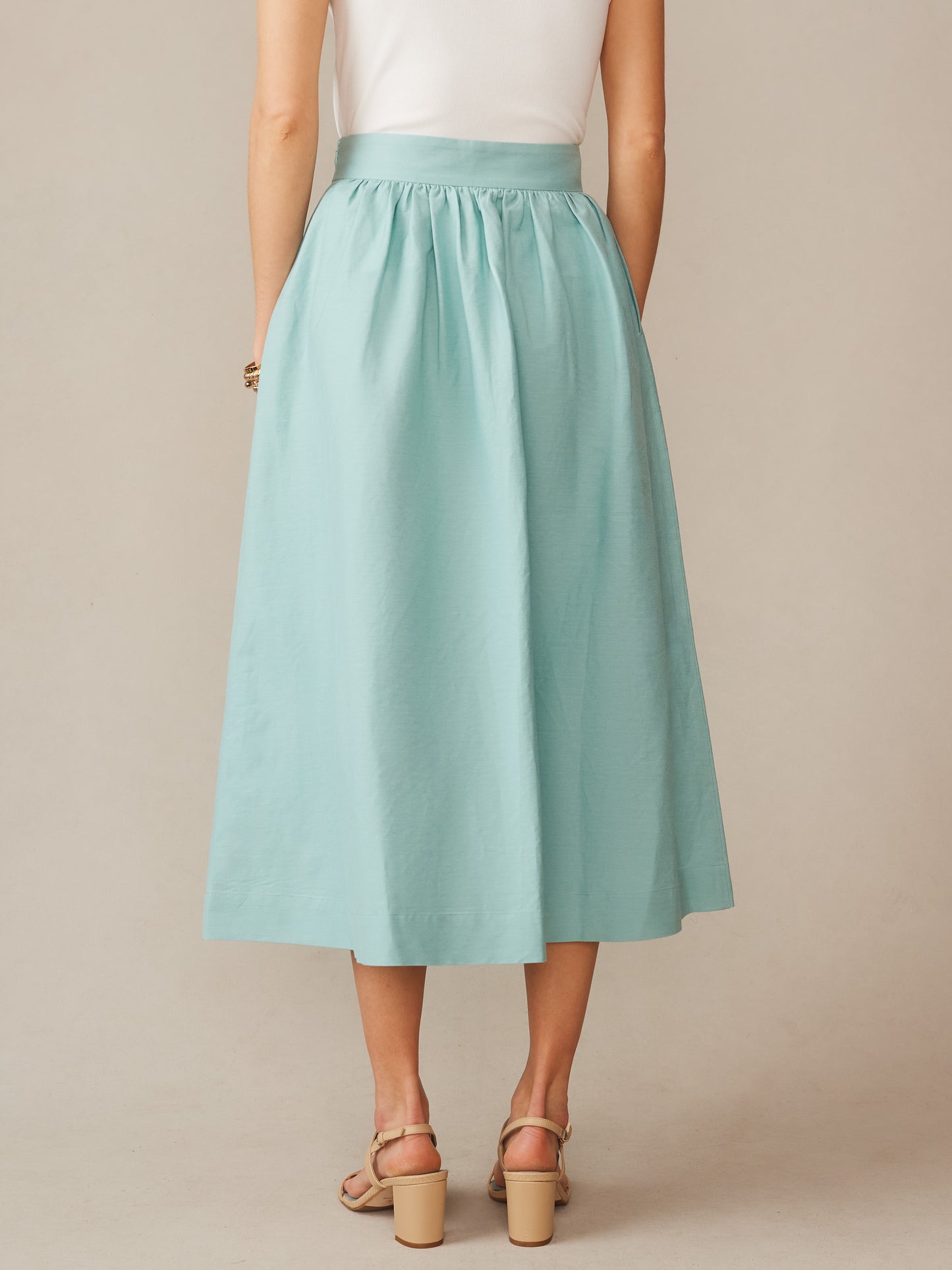 Back view of a woman wearing a seafoam green Winnie Linen Blend Skirt by J.McLaughlin, paired with a white top and beige heeled sandals, showcasing effortlessly stylish, enduring designs and innovative fabrics at a destination for defining style. Life, Well-Lived.
