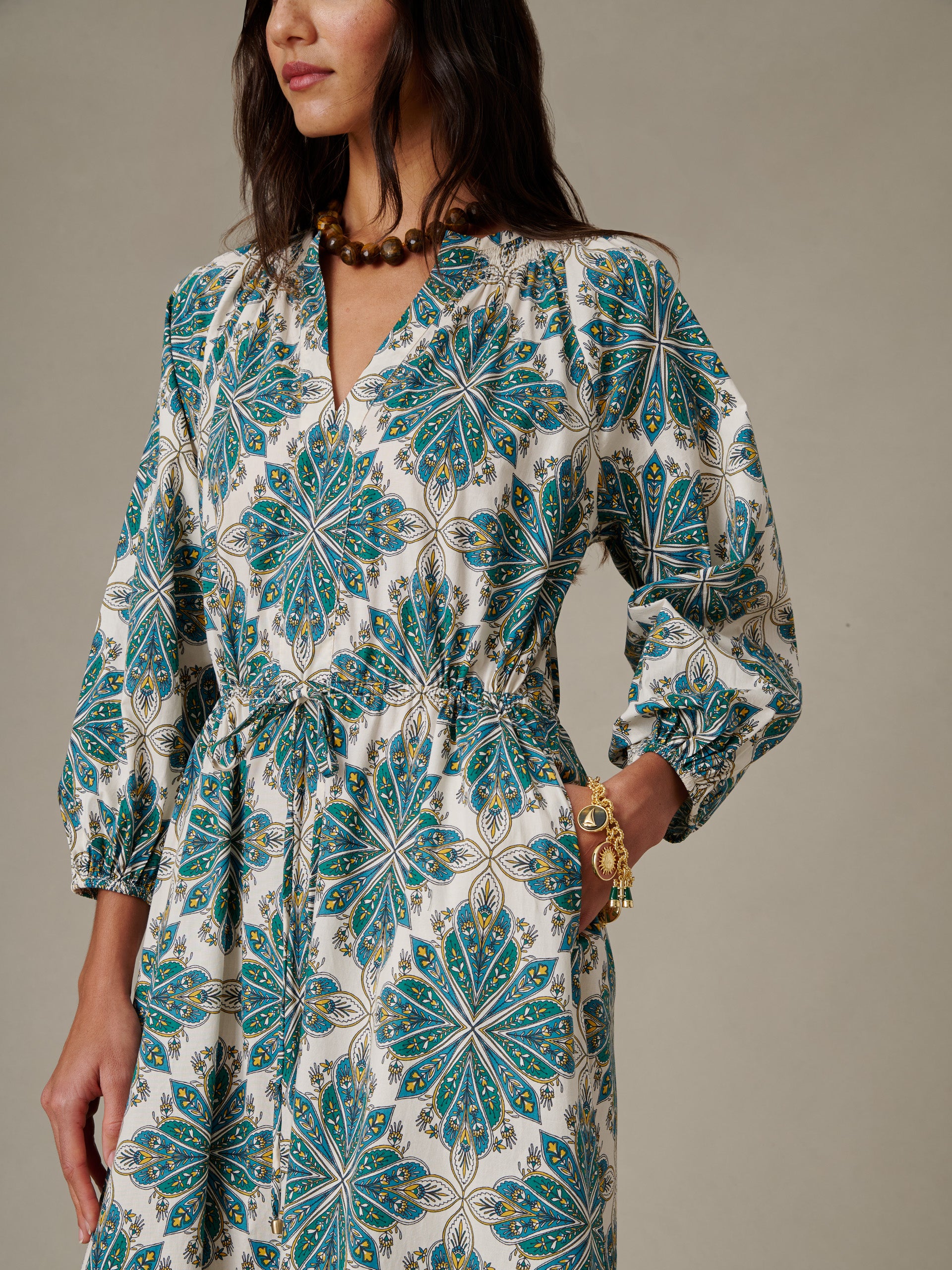 Woman wearing a patterned Winslet Dress in Neo Radiant by J.McLaughlin, featuring long sleeves, cinched waist, and a vibrant blue and green floral design.